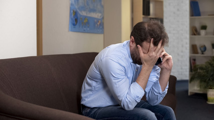 Upset male on couch talking to boss on smartphone, problems, losing job