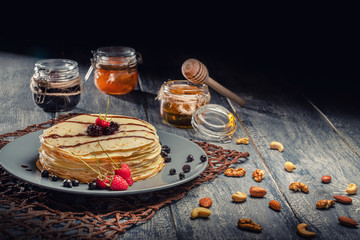 Delicious pancakes with fresh fruit on dark wooden background, served with honey and jam in glass bowl