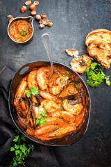 Traditional Catalan fish stew romesco de peix with prawns, mussels and fish as top view in a modern...