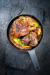 Traditional barbecue leg of lamb with lemon and tomatoes as top view in a cast-iron skillet