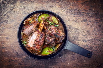 Traditional barbecue leg of lamb with lemon and tomatoes as top view in a cast-iron skillet