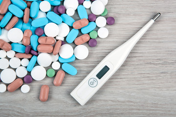 background of many multi-colored medical pills and a thermometer top view