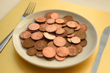 Pence coins on white plate on gold background with cutlery