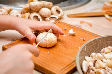 Children's small hands, a knife, shampions and a frying pan. The child cuts champignons.