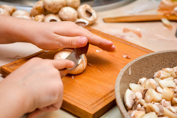 Little children`s hands chops champignons mushrooms. Cooking at home.