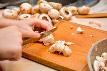 Cooking at home. The child cuts champignons. Children's hands with a knife close-up - cuts mushrooms.
