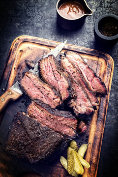 Traditional smoked barbecue wagyu beef brisket as piece and sliced offered as top view on an old cutting board with Louisiana sauce - vintage