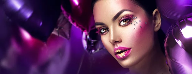 Tuinposter Schoonheid fashion model meisje creatieve kunst make-up met edelstenen. Vrouw gezicht over paarse, roze en violet lucht ballonnen achtergrond © Subbotina Anna