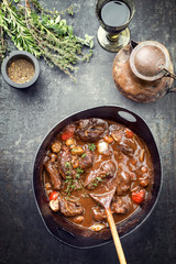 Traditional German braised pork cheeks in brown sauce with mushroom and carrots as top view in a cast-iron pot