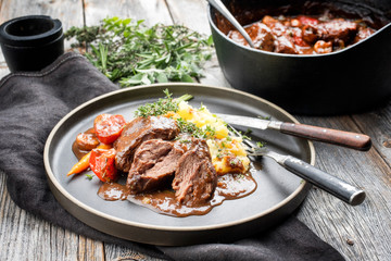 Traditionelle geschmorte Schweinebäckchen in brauner Rotwein Sauce mit Pilzen, Karotten  und Kartoffel Püree als closeup auf einem Modern Design Teller
