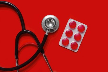 Stethoscope and medicine pills on red background with copy space.