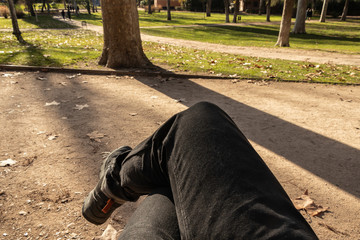 POV of a man legs crossed sitting on a bench in an outdoor park