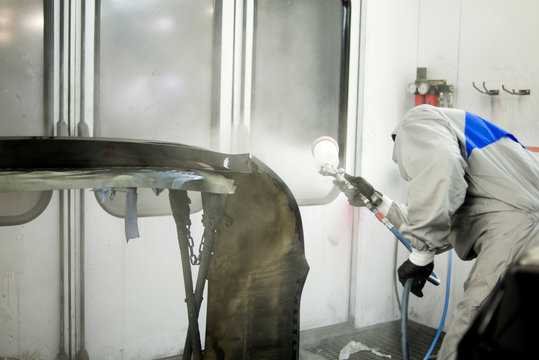 Mechanic in Painting Booth spray the hood of a car