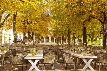 Munich, Germany - fine weather in November, we can still eat outside! A beer garden is ready for guests under a cover of golden leaves at Hofgarten in central Munich
