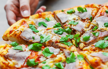 woman Hand takes a slice of Pizza with Mozzarella cheese, ham, pepper, meat, Tomato sauce, Spices and Fresh Basil. Italian pizza on wooden background
