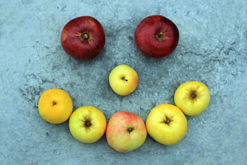 Funny smile of red, yellow and green apples on a gray metallic background. 