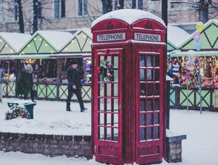 Fototapeta premium Christmas holidays concept of red classic English phone booth, season winter fair with people background in snowing weather 