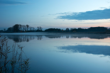 Fog on the lake and trees on the shore reflecting in the water