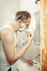 Aging man in a-shirt shaving face with old style razor