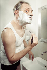 Aging man in a-shirt shaving face with old style razor
