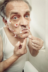 Aging man in a-shirt shaving face and cut himself with old style razor