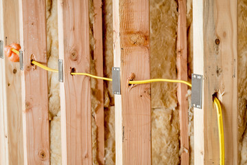 Yellow wire fed through wood studs in new home construction with steel protector plates