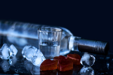 A bottle of vodka and a glass with ice, alcoholic drink, close-up on a black background