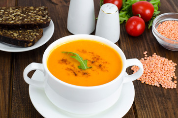Red lentil soup in plate on wooden background