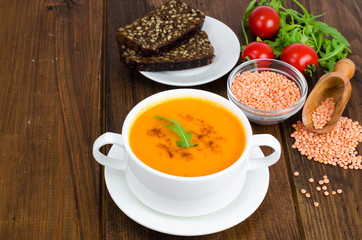 Red lentil soup in plate on wooden background