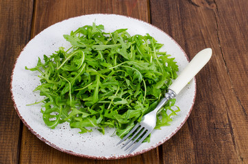 Vegetarian dish, plate with green arugula on wooden table
