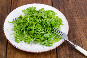 Vegetarian dish, plate with green arugula on wooden table