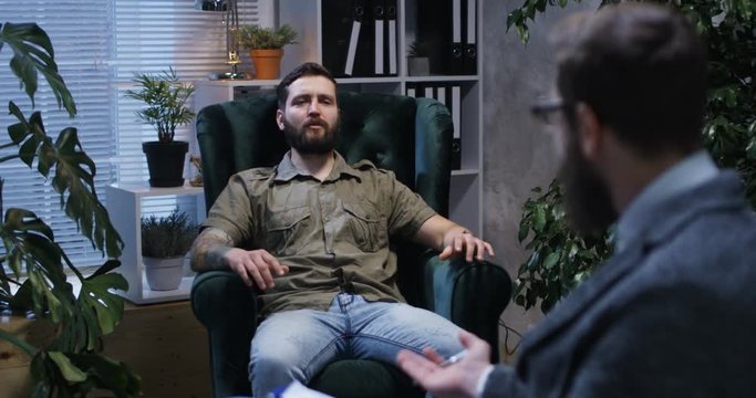 Medium shot of young man listening and talking to a male psychologist