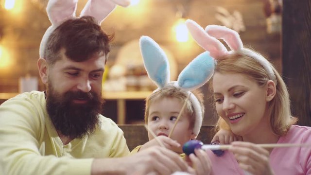 Father, mother and kid boy painting Easter eggs. Happy family are preparing for Easter. Cute little child boy wearing bunny ears. Easter eggs on wooden background.
