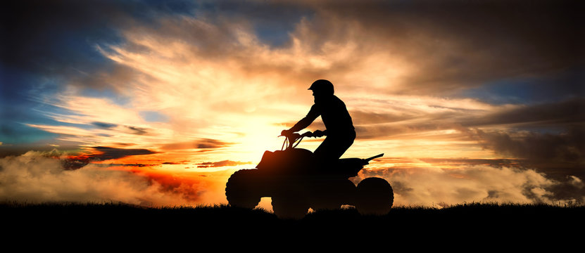 Young man rides an ATV over background of mountains at sunset
