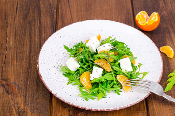 Delicious fruit and vegetables salad. Tangerine, feta cheese, arugula and chia seeds in plate. Healthy food concept