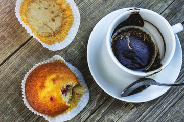 On a wooden table is an empty Cup of coffee and a bitten cake