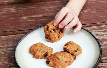 child stealing a pumpkin chocolate chip cookie from a plate.