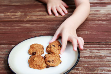 child stealing a pumpkin chocolate chip cookie from a plate.