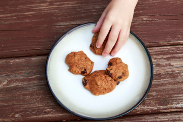 child stealing a pumpkin chocolate chip cookie from a plate.