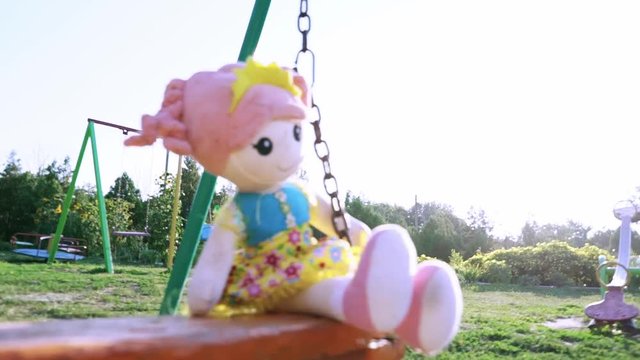 Baby doll on swing. The toy falls from the swing. The abandoned toy on the playground.