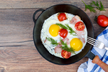 Frying pan with fried eggs, bacon and tomatoes