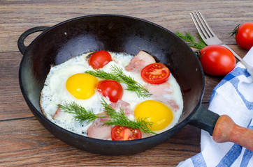 Frying pan with fried eggs, bacon and tomatoes