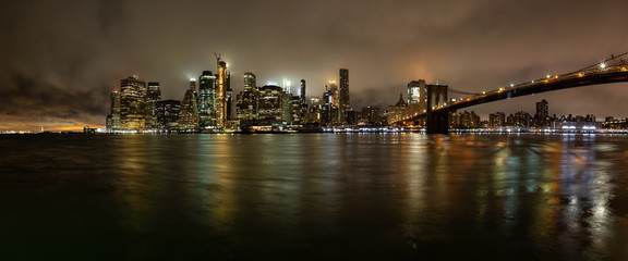 Panoramic view of the Downtown Manhattan and Brooklyn Bridge during a foggy night. Taken in New York, NY, United States.