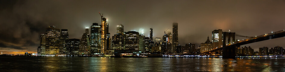 Panoramic view of the Downtown Manhattan and Brooklyn Bridge during a foggy night. Taken in New...