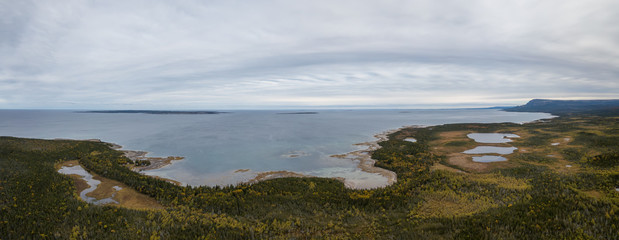 Aerial panoramic view of a scenic road near the Atlantic Ocean Coast during a cloudy morning. Taken in Newfoundland, Canada.