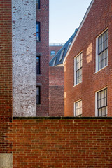 A group of brownstone buildings stand in a court yard. One building has traditional multi-paned windows with white frames. A large vertical white painted brick wall stands near the left center.