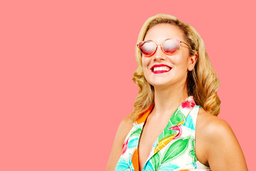 Smiling blonde woman with red sunglasses and summer dress, isolated on pink studio background