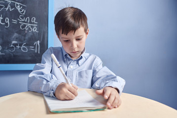 Diligent Caucasian schoolboy is trying to solve difficult task at school. He is sitting at the desk and writing.