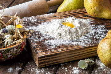 Close up. Cooking traditional pear cake. Making dough from quail eggs and flour on a brown wooden board.