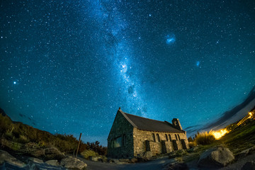 An abandoned house under the beautiful night sky. There are stars and milky way. This is a famous tourist destination in New Zealand. This image has star trail to show the earth rotation.